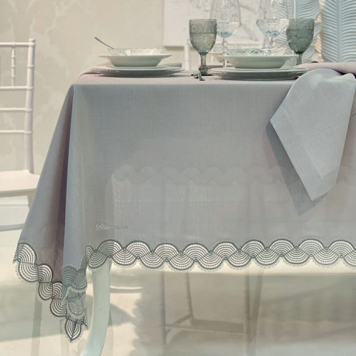 Tovaglia Callas Blumarine 180x300 cm su tavola apparecchiata con pizzo decorativo sui bordi e logo ricamato